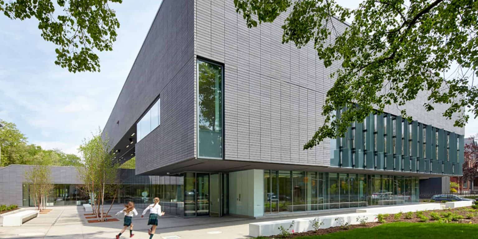 Modern school building with sleek design and large windows, surrounded by greenery.