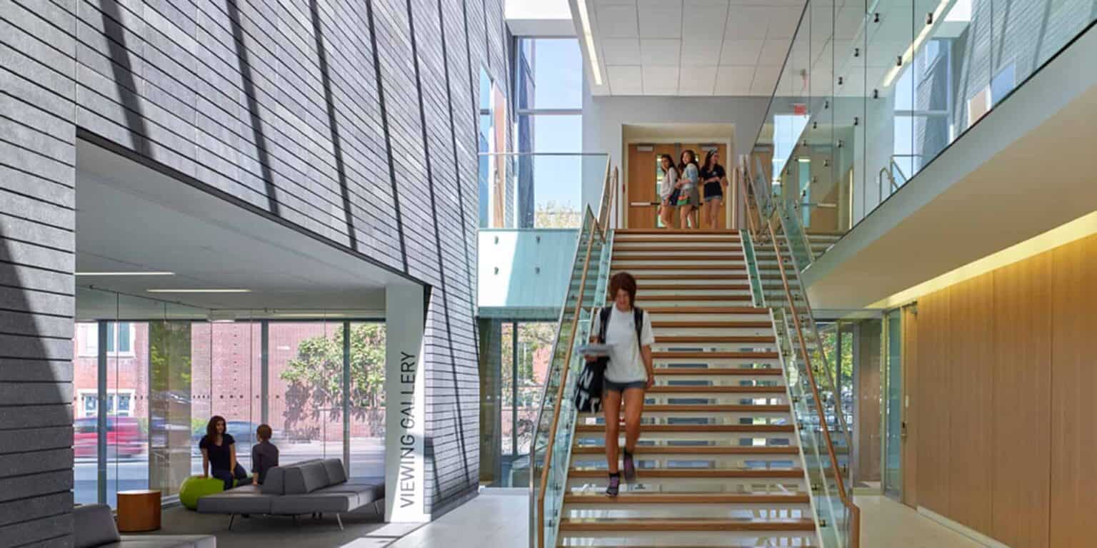 Bright modern school interior with students at staircase and lounge area, showcasing innovative education environment.