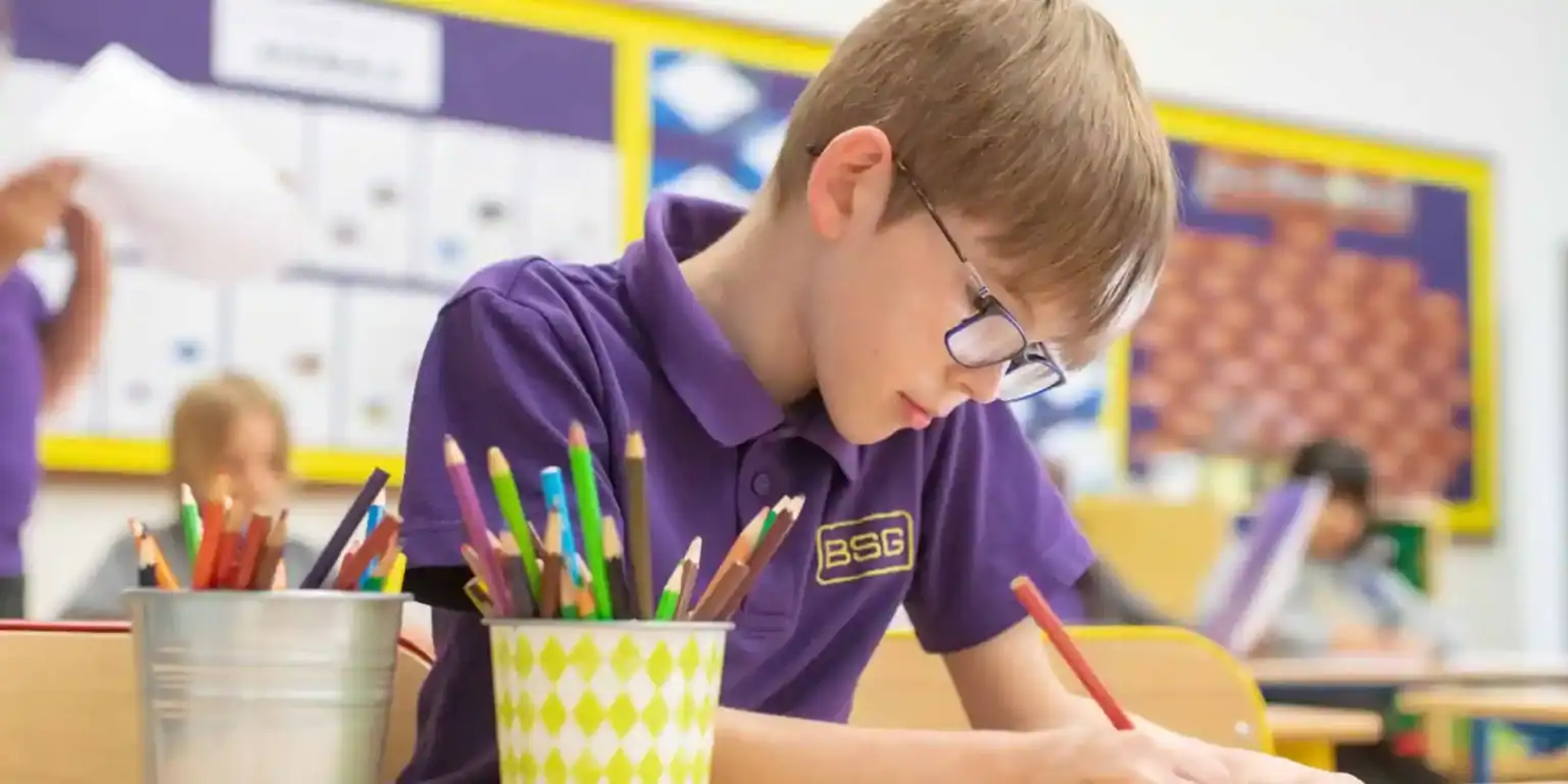 Studente colorato concentrato sui compiti scolastici con matite in classe.