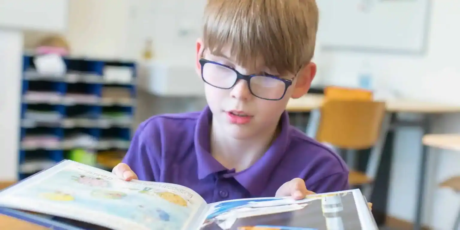 Bright young student reading a colorful educational book in a modern classroom.
