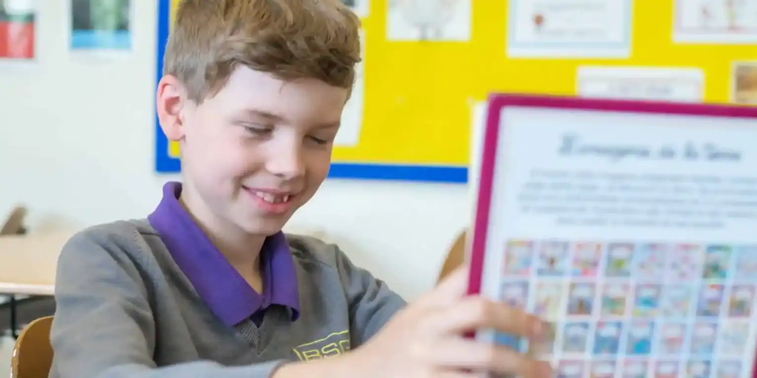 Bright young student reading colorful educational material in classroom for World Schools SEO.