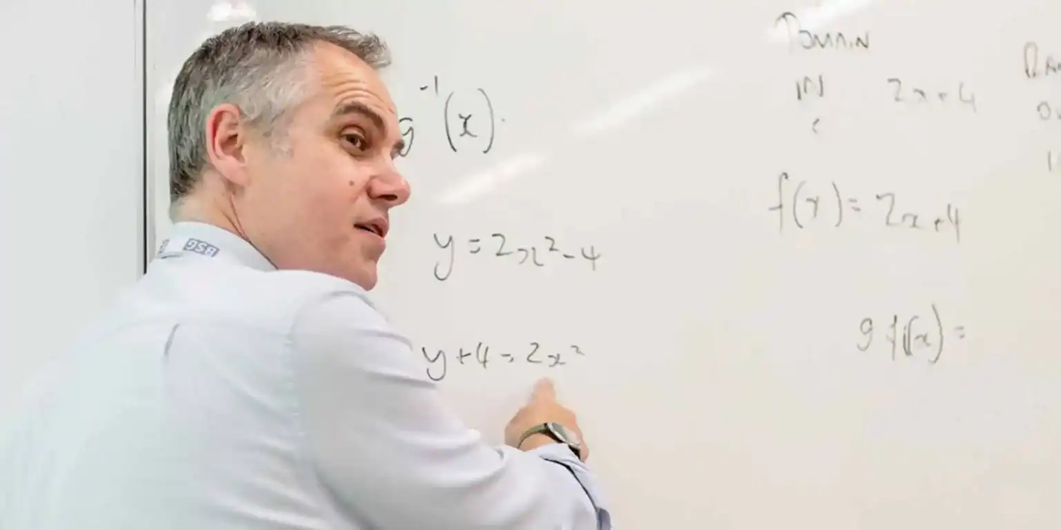 High school teacher explaining algebra equations on whiteboard for students.