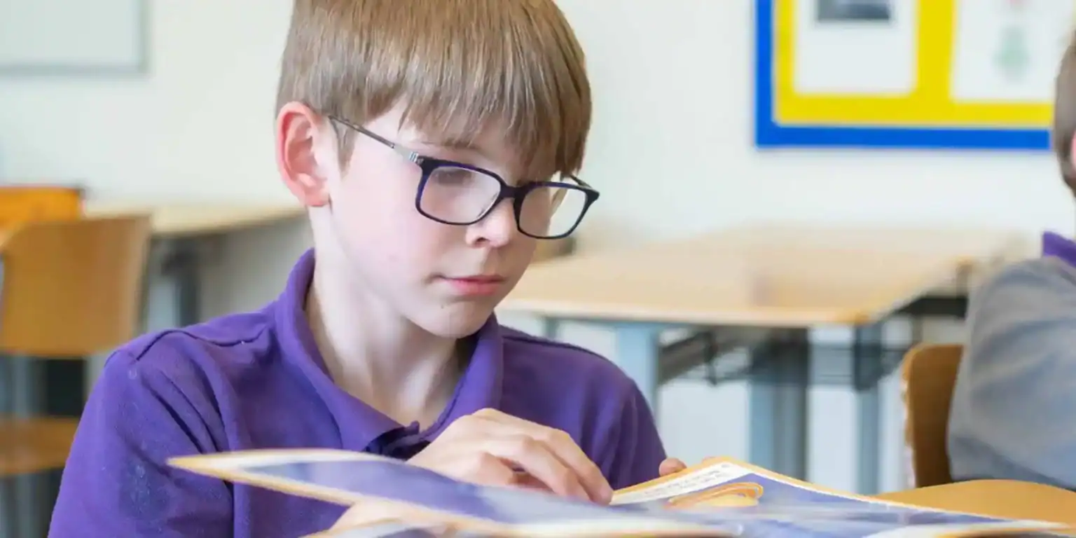 Bright schoolboy studying with a book in a classroom, focusing on education at an international school.