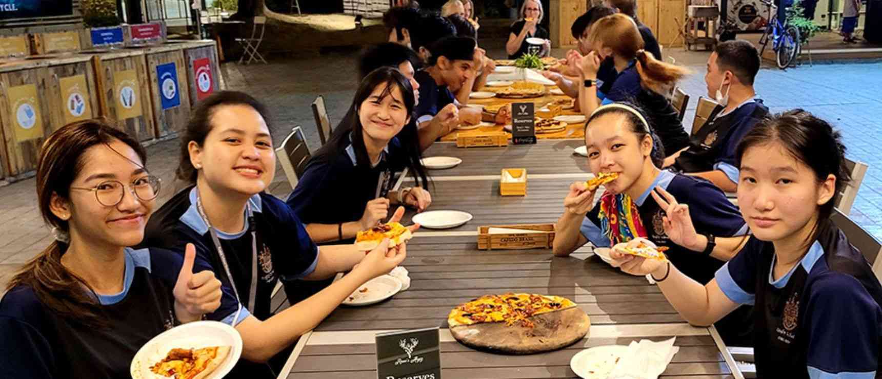 Delicious pizza enjoyed by diverse students at outdoor school event, fostering community and cultural exchange.