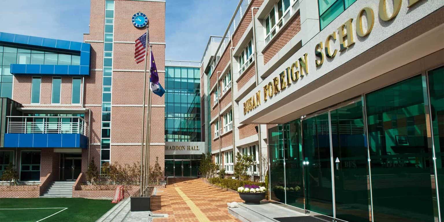 Modern world school campus with brick facade, glass entrances, and flags, providing a global education environment.