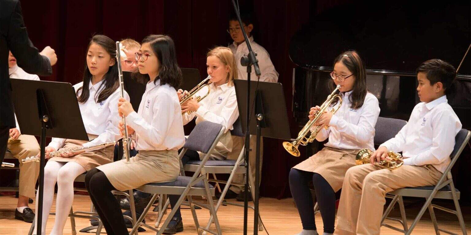 Bright young students performing with musical instruments in a school orchestra on stage.