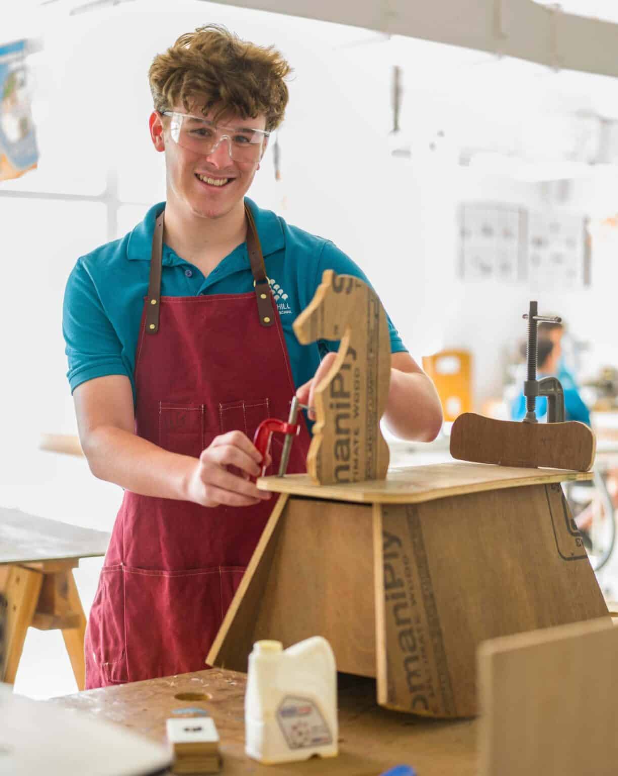 Young male student assembling a woodworking project in a school workshop.