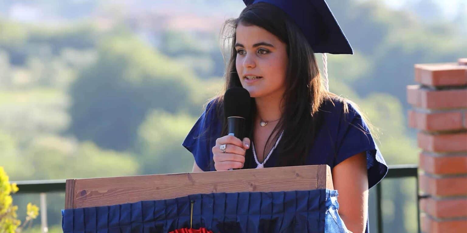 Graduate girl giving speech at outdoor graduation ceremony, emphasizing academic success and student achievement.