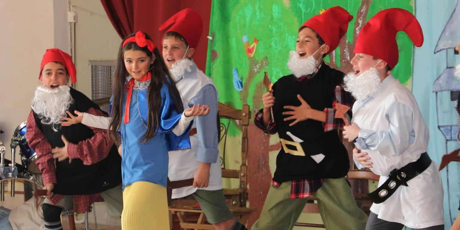 Joyful children performing a play in colorful costumes at a school event.