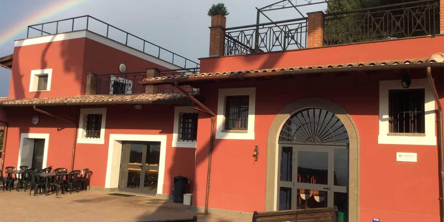 Bright red school building with outdoor seating area and rooftop terrace, located in Italy.