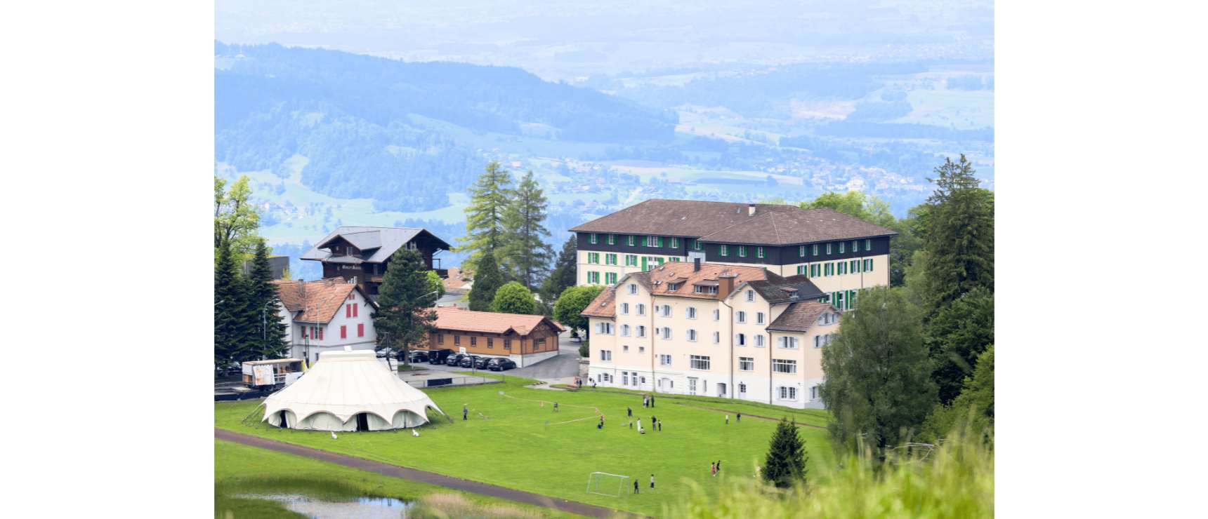 Elegant school campus with traditional architecture nestled in lush greenery and scenic mountains.