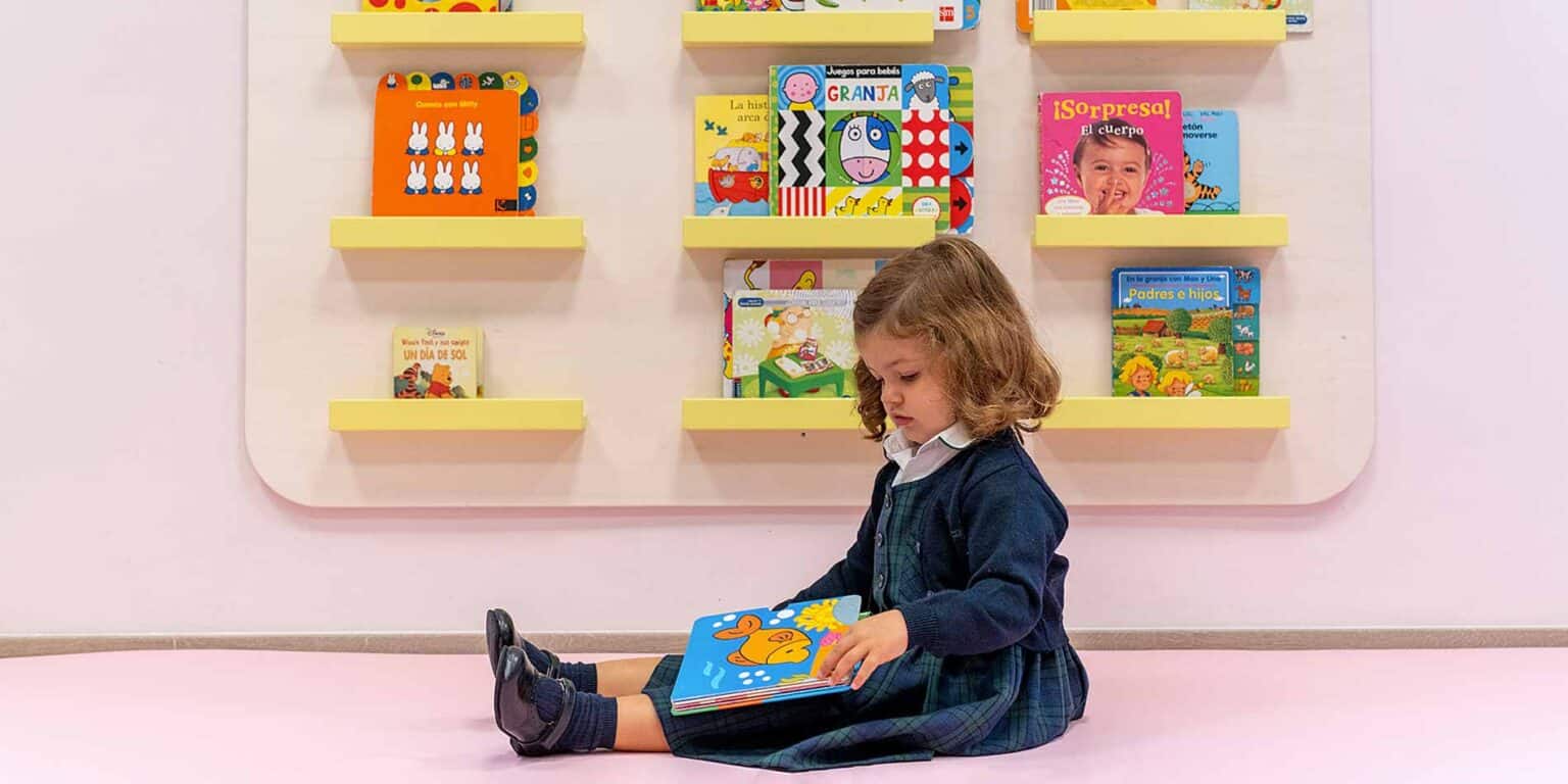 Colorful children's books displayed on yellow wall-mounted shelves at a modern preschool.