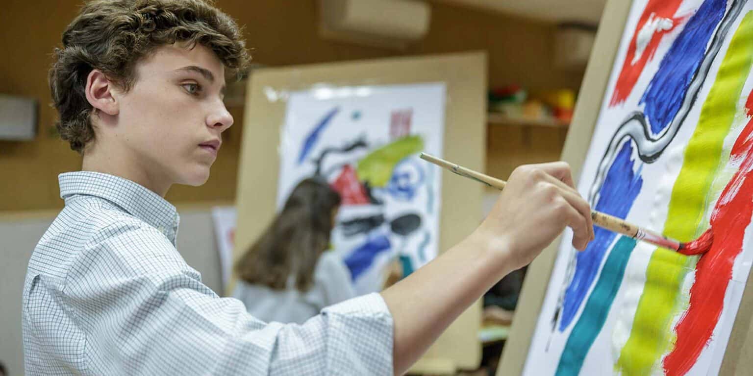 Bright young student painting colorful abstract artwork at art class, promoting creative education.