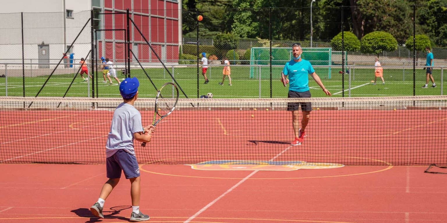 Child playing tennis with coach on outdoor court at World Schools.