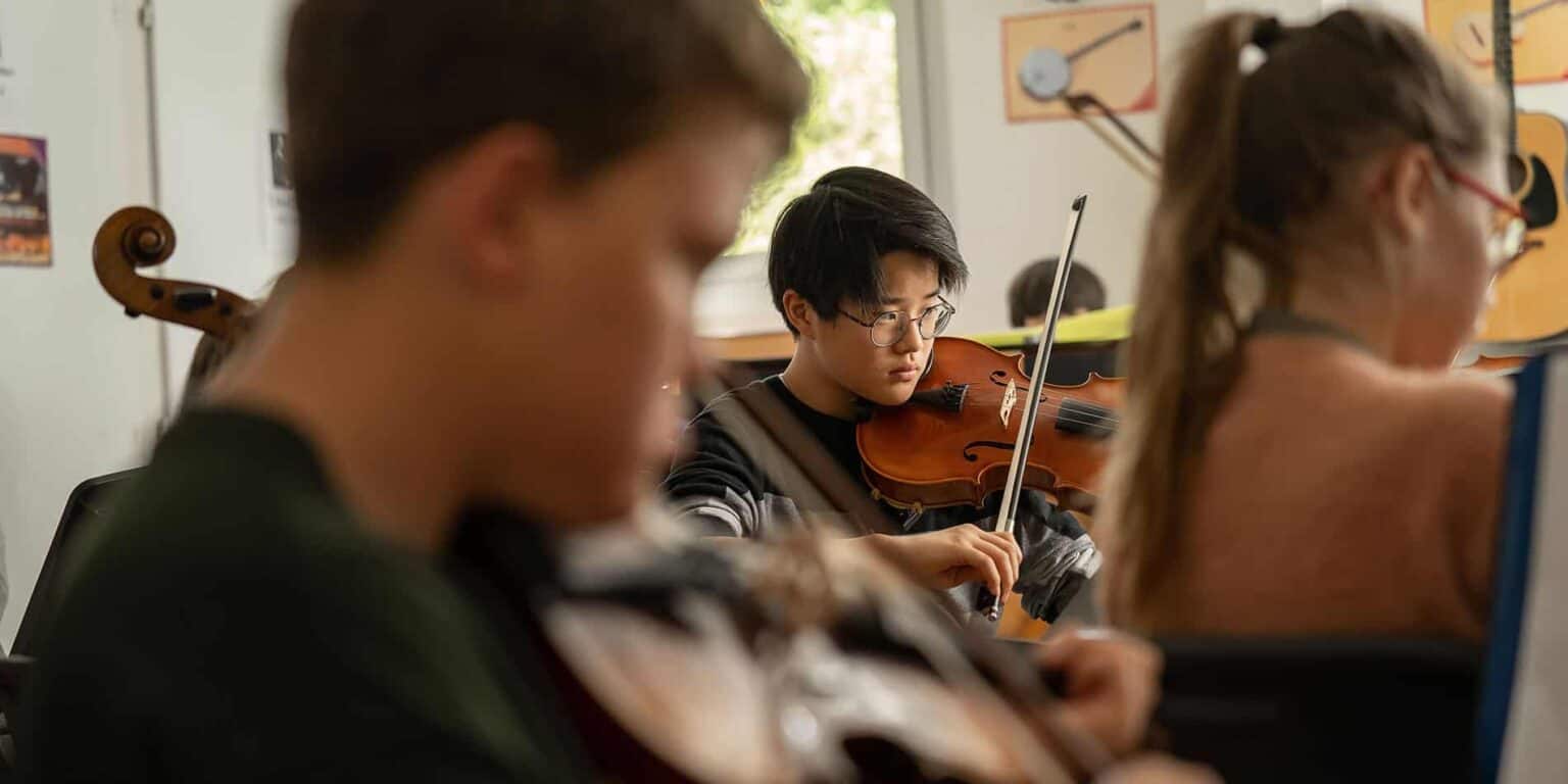 Focused student playing violin in music classroom at World Schools.