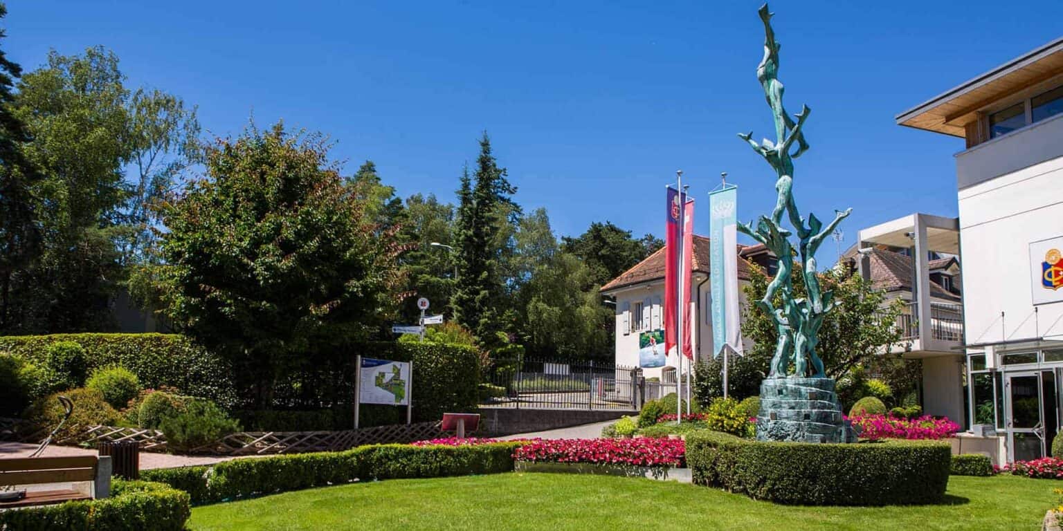 Modern international school entrance with sculptures and lush greenery in a serene campus setting.