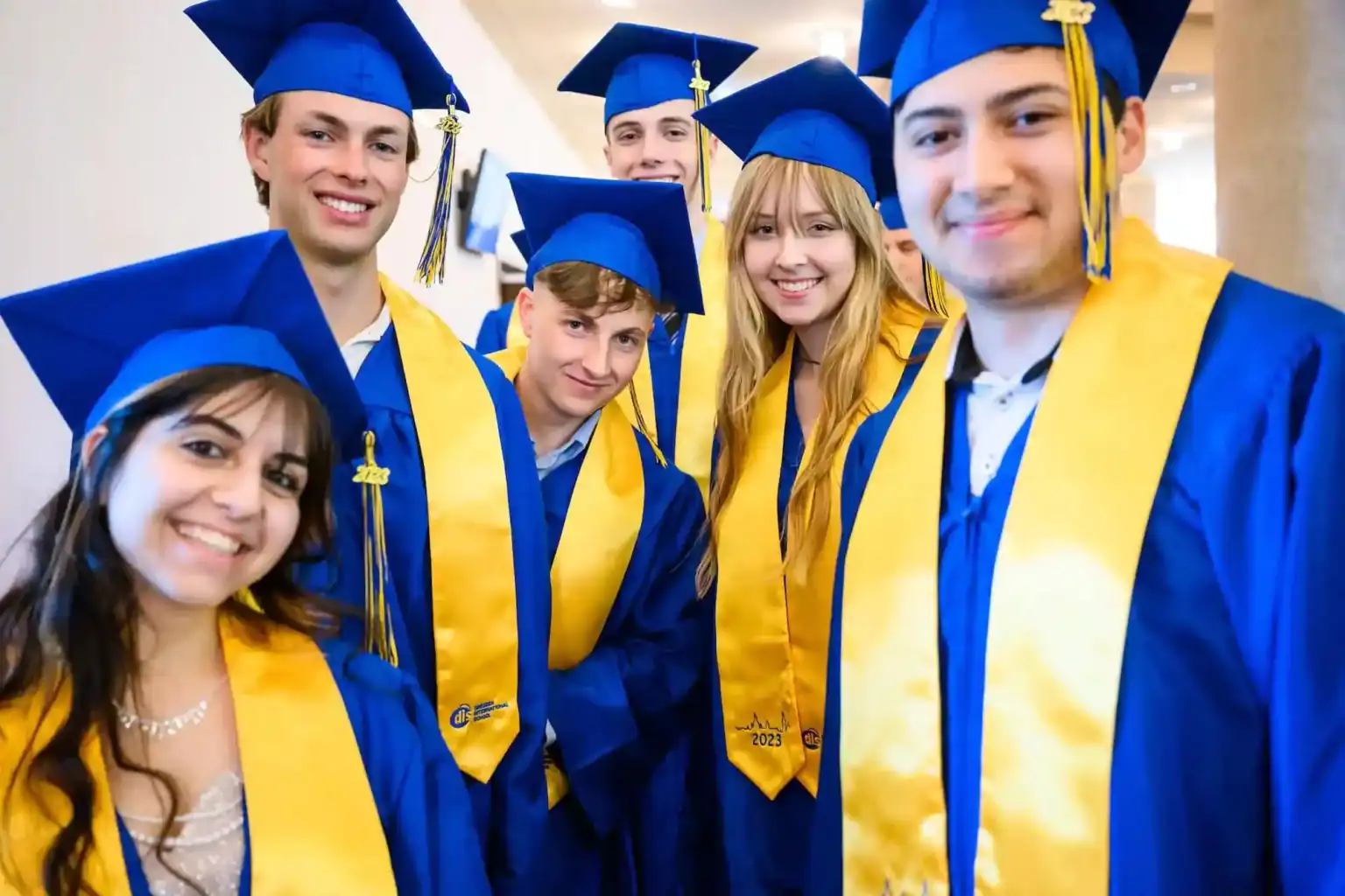 Smiling graduates in blue and yellow caps and gowns celebrating graduation at an international school.