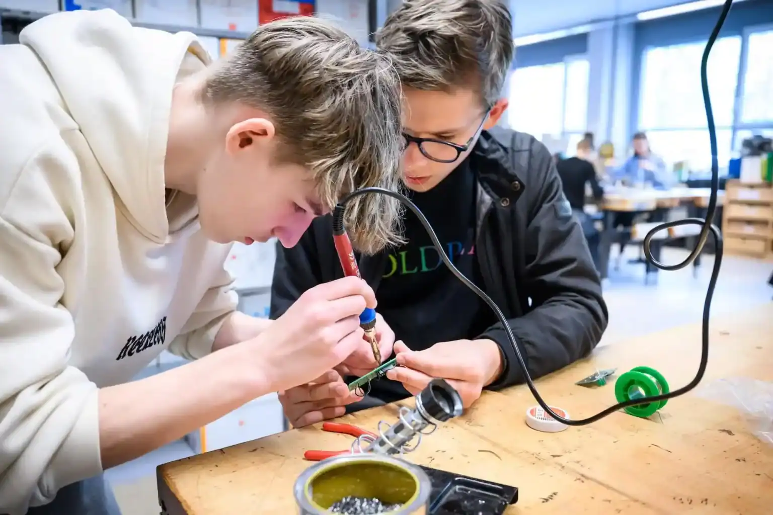 Youth students engaged in hands-on electronics and soldering work at a modern school laboratory.