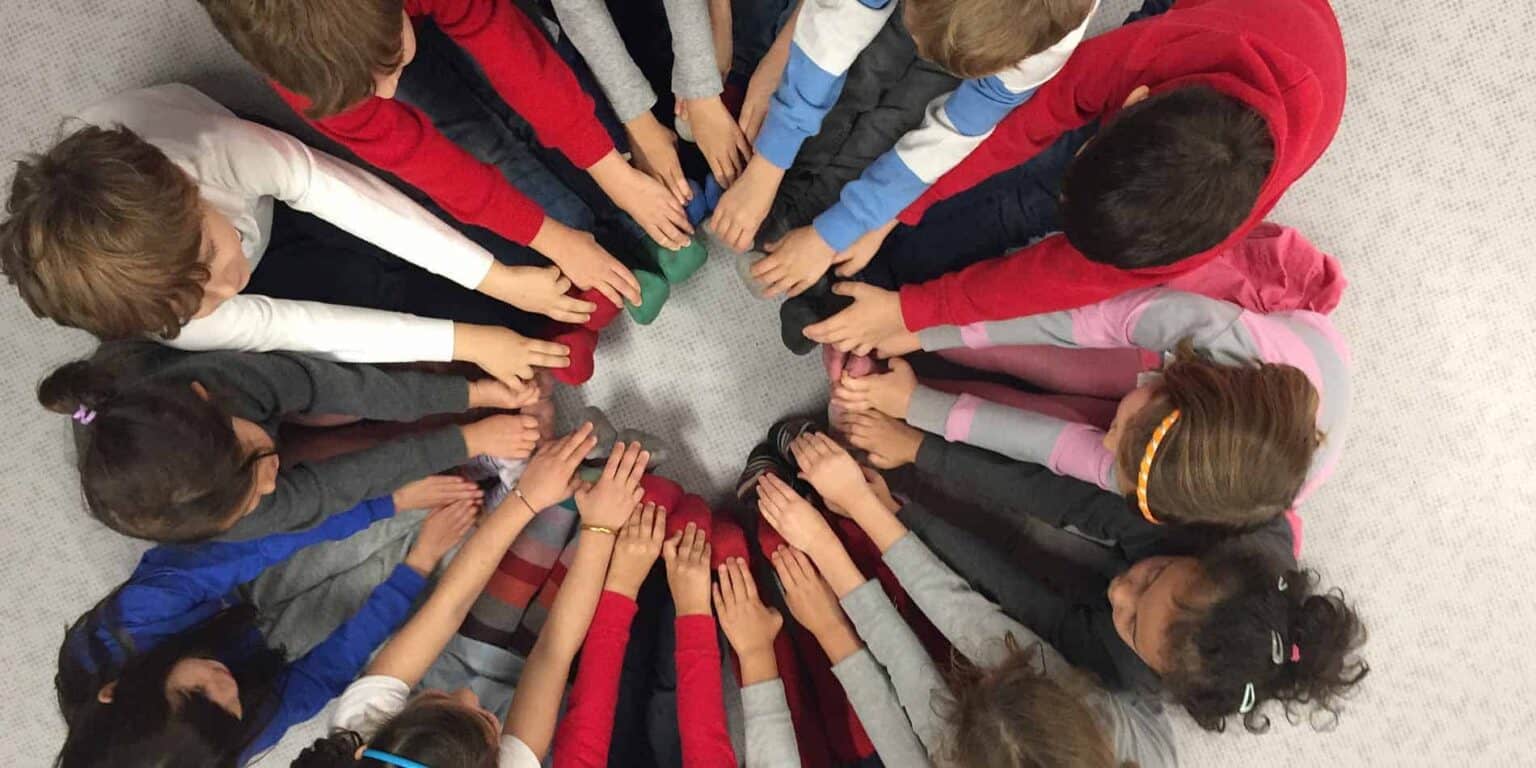 Diverse children forming a circle with hands in the center, symbolizing teamwork and collaboration at World Schools.