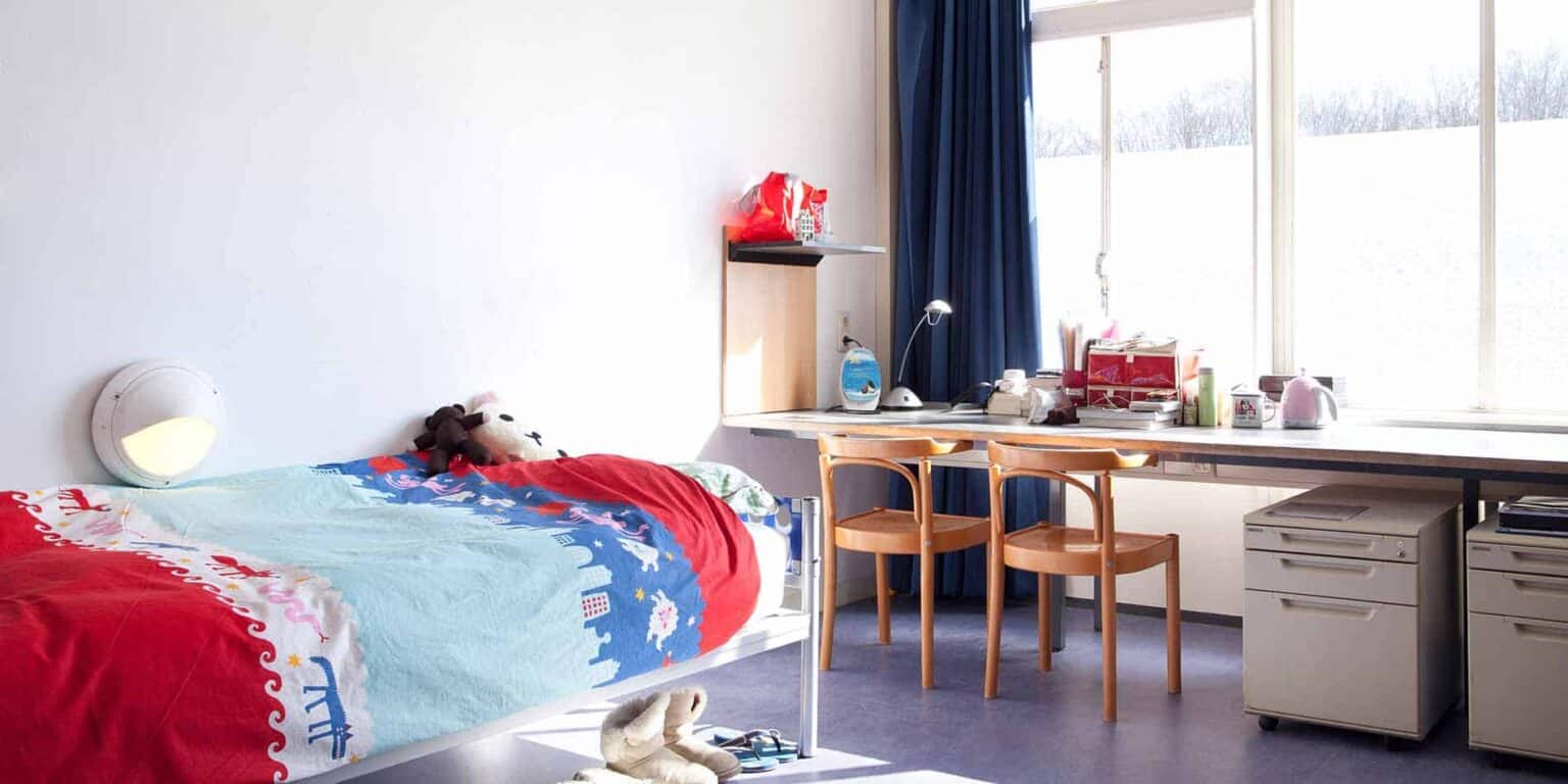 Cozy student dorm room at World Schools with single bed, study desk, and bright window for optimal learning environment.