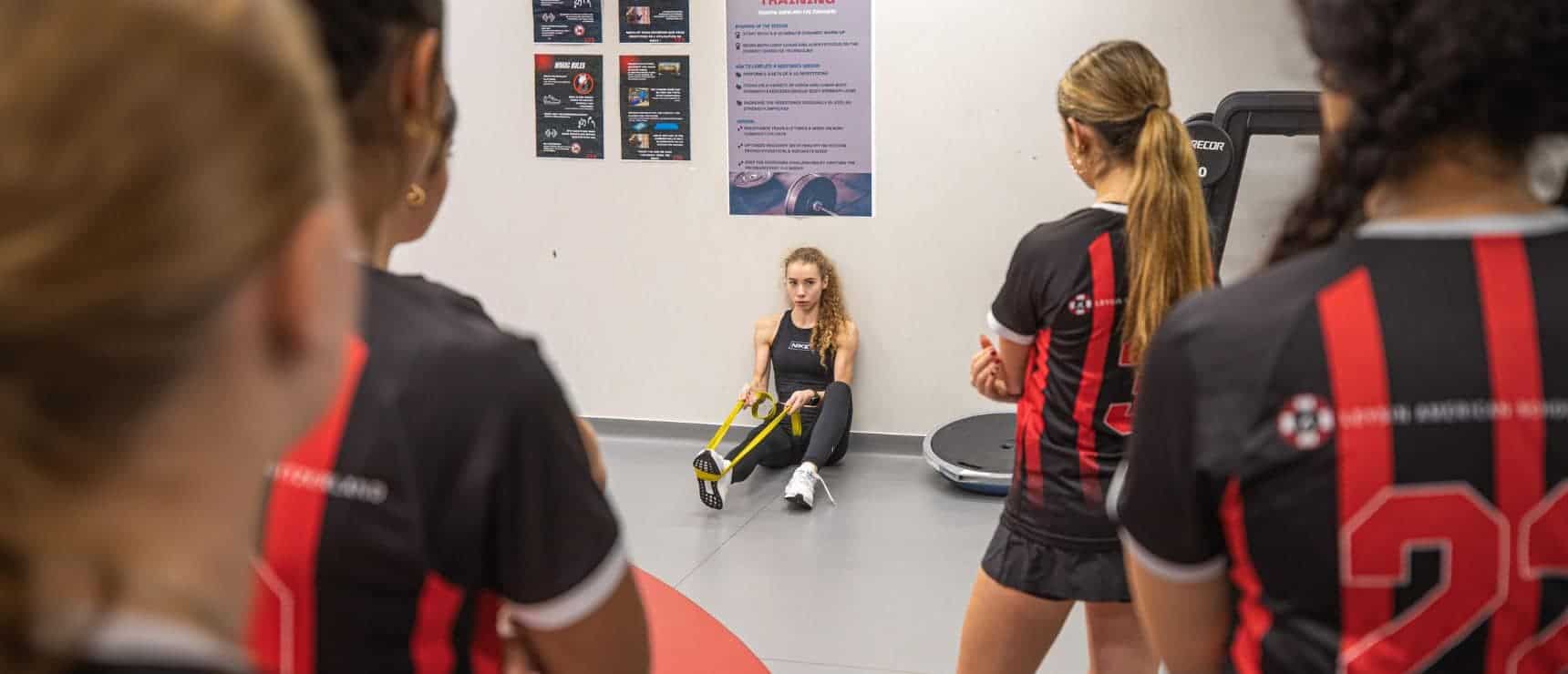 High school athletes training indoors at a sports facility with coaching and fitness equipment.