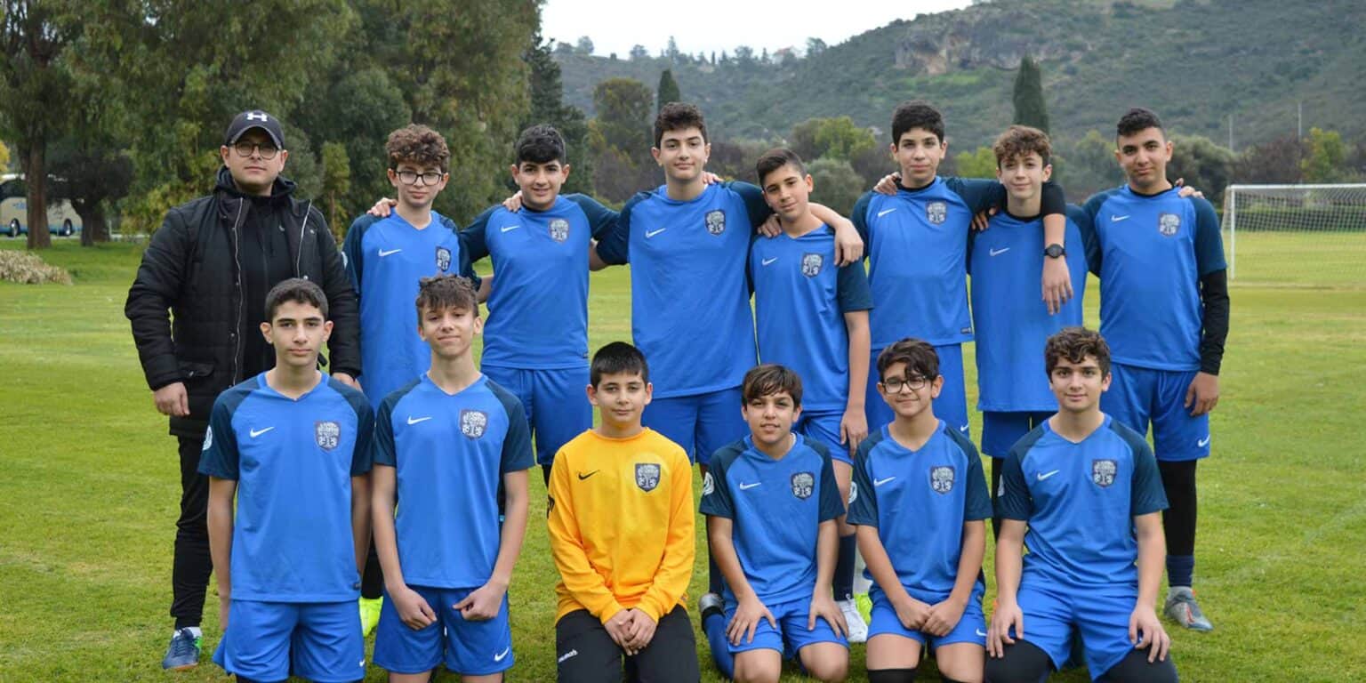 Youth soccer team students in blue uniforms with coach on school sports field.