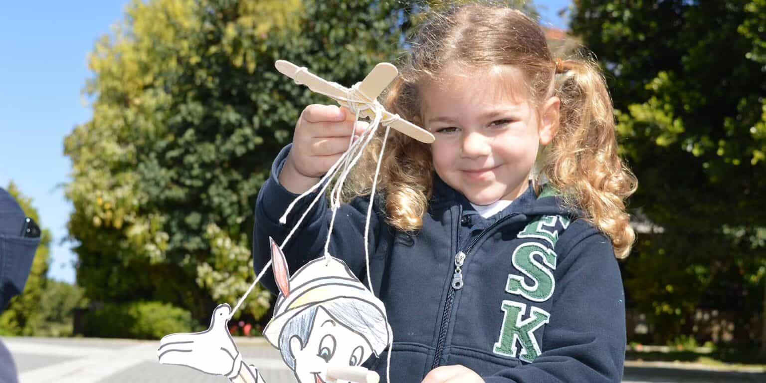 Colorful schoolgirl displaying handmade puppet outdoor during fall, emphasizing creativity and learning environment.