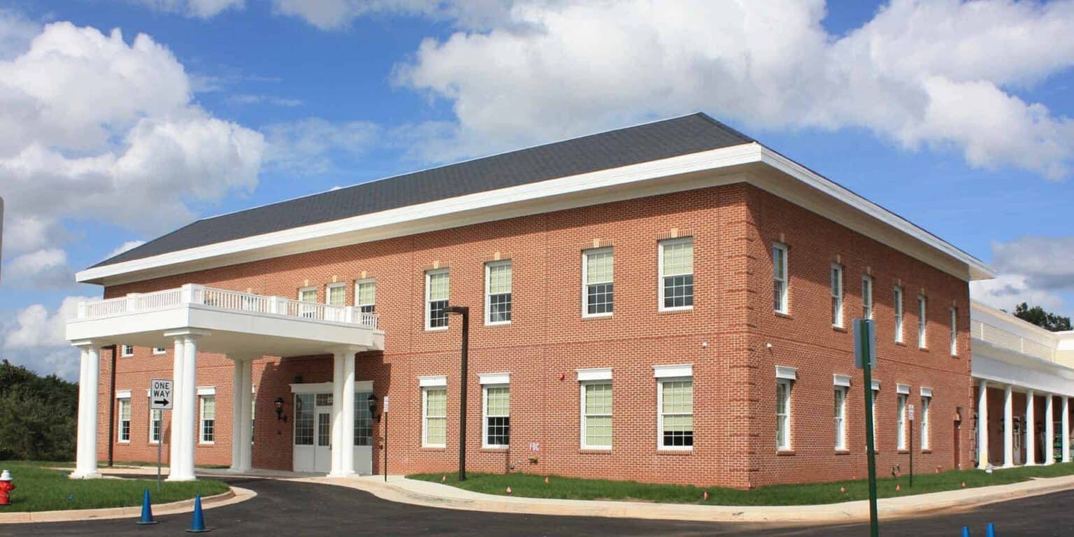 Edifício escolar moderno em tijolo com colunas brancas e grandes janelas sob um céu parcialmente nublado.