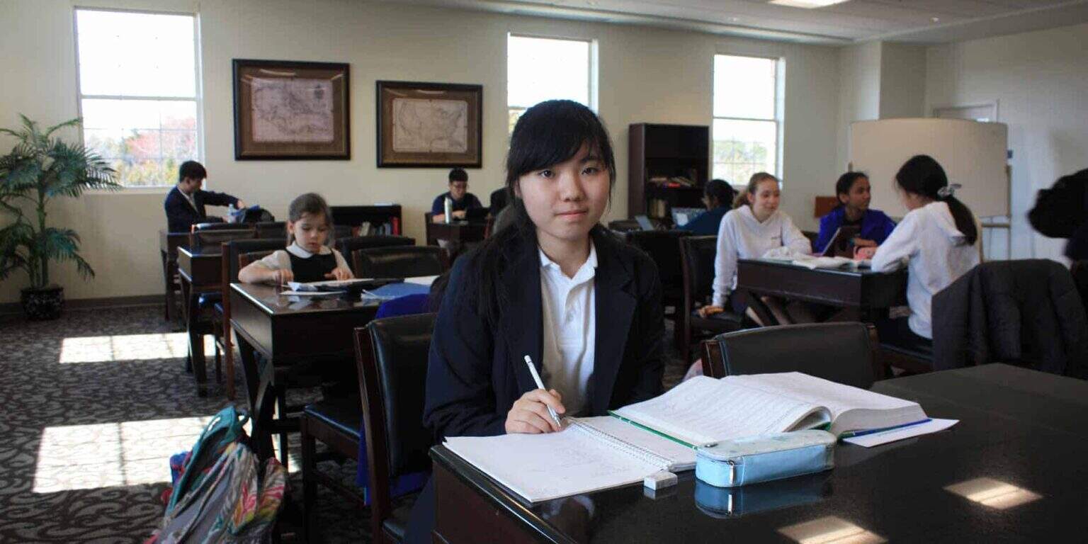 Young diverse students studying in a classroom with books, laptops, and whiteboard for international education.