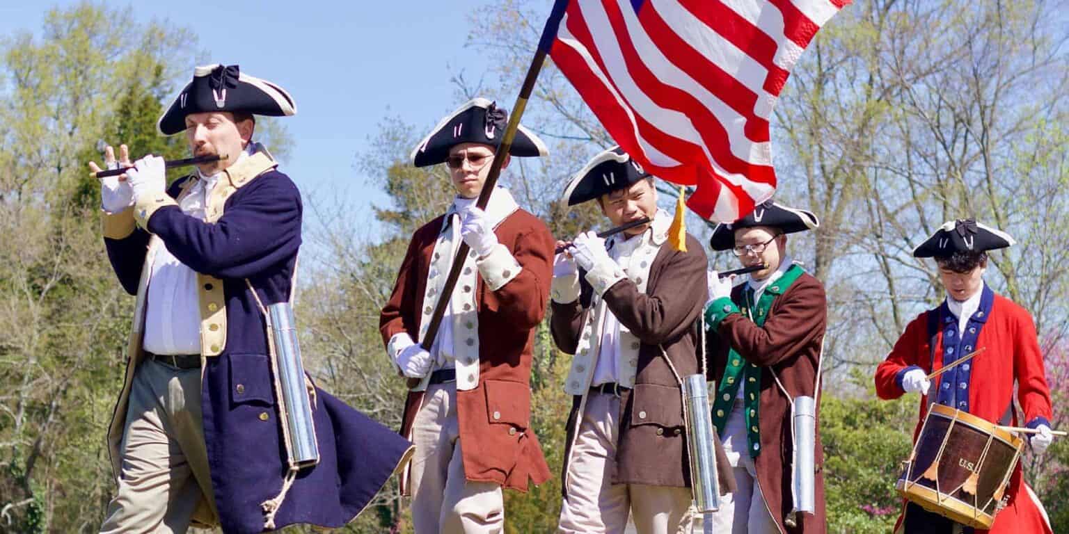 Children dressed as colonial soldiers performing during a historical reenactment, promoting cultural education at World Schools.
