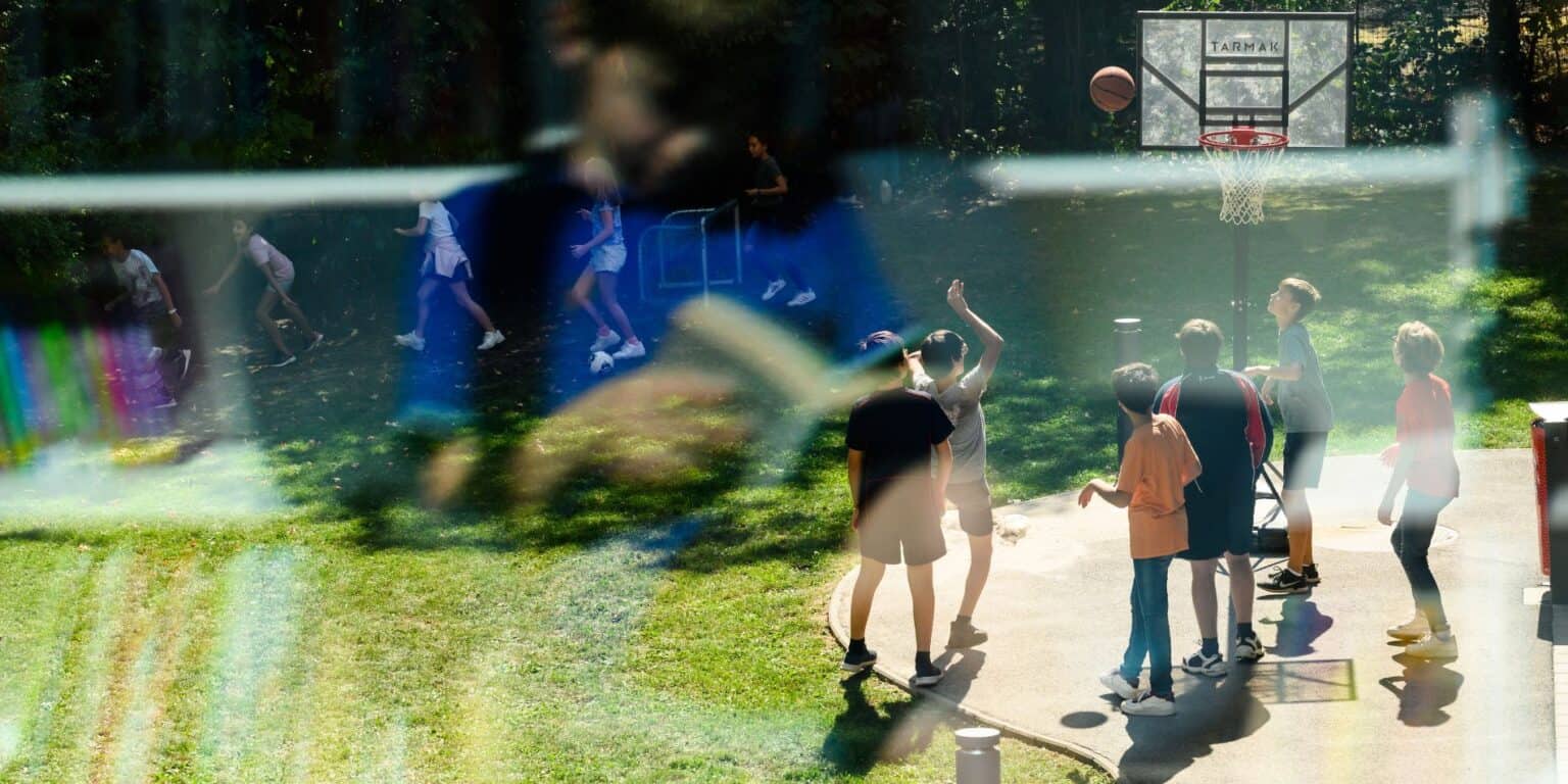 Children playing basketball outdoors at a school sports court.