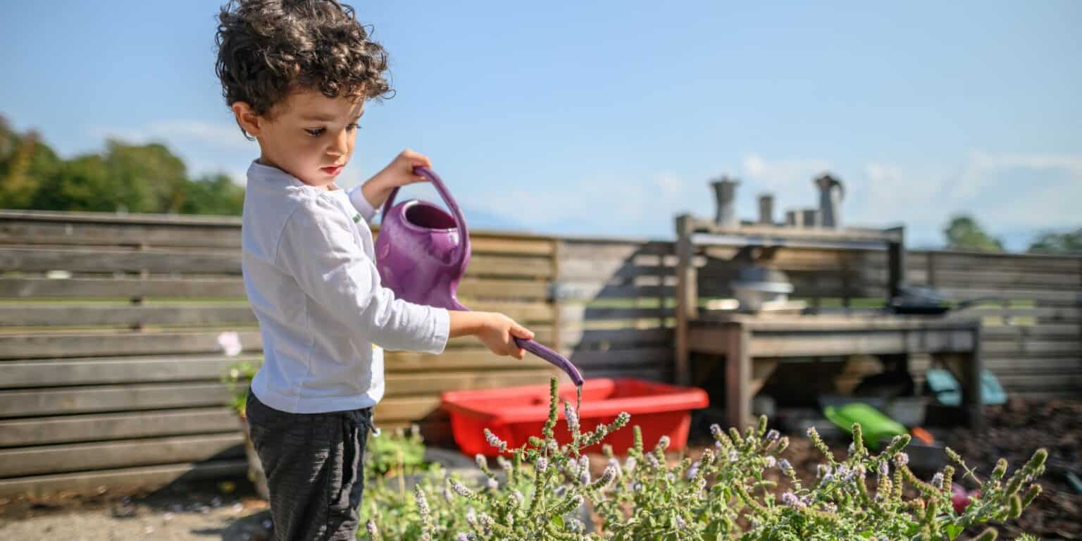 Child watering garden plants at a school outdoor playground, promoting sustainability and environmental awareness.
