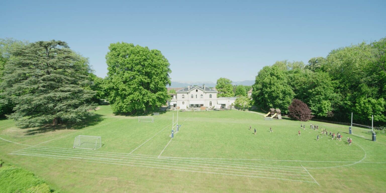 Lush green school grounds with sports fields and a grand white building, ideal for international student life and activities.