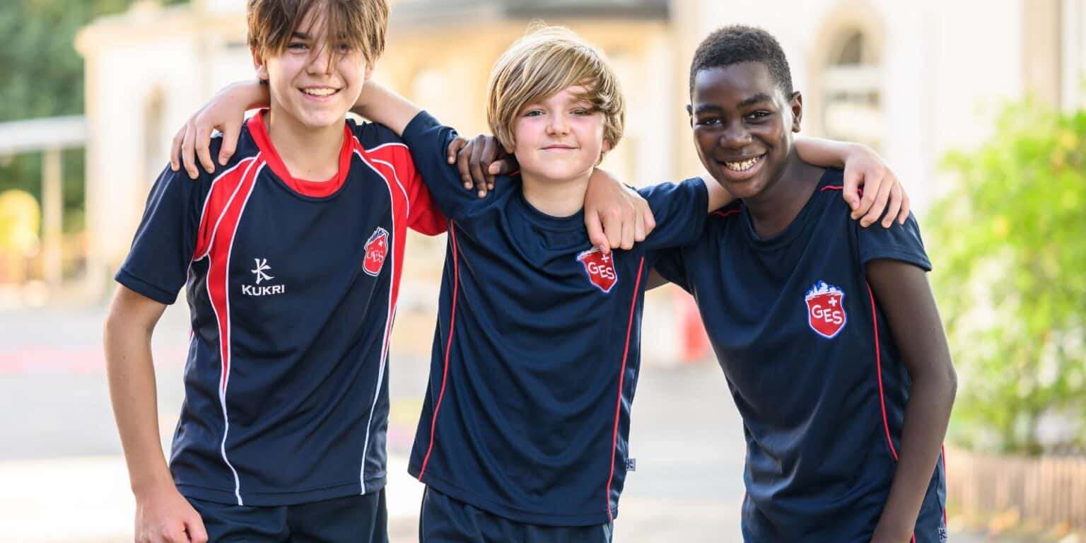 Smiling diverse schoolboys in sports uniforms with arms around each other outdoors.