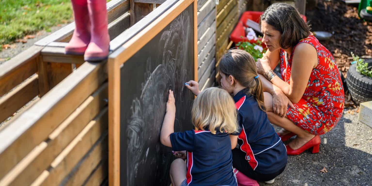 Smart kids drawing on outdoor chalkboard at a garden schoolyard during daytime.