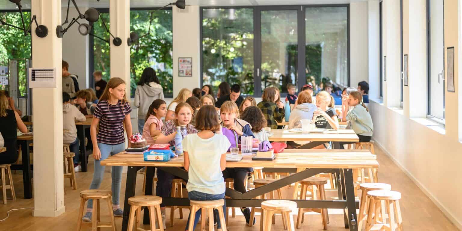 Bright, modern school cafeteria filled with students enjoying lunch in a well-lit environment with large windows, perfect for learning and community.