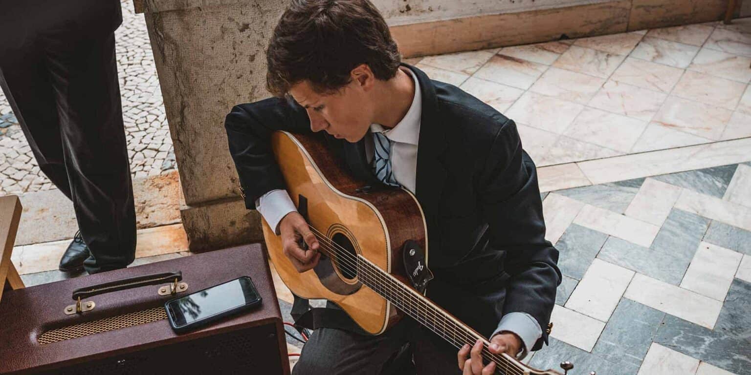 Young man playing acoustic guitar outdoors at a school event, showcasing student talent and arts education in international schools.