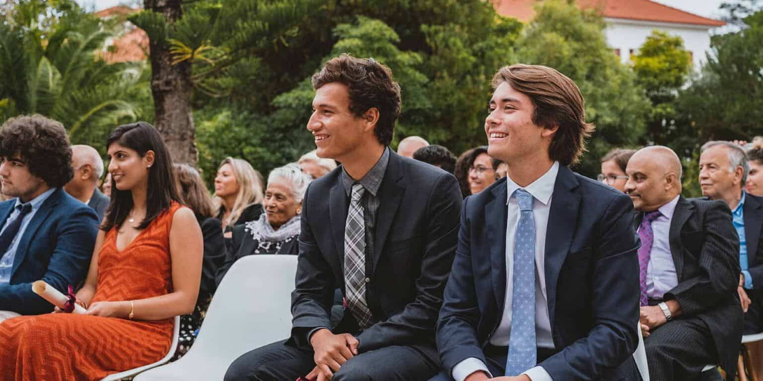 Diverse students in formal attire attending an outdoor school event at a lush green campus.
