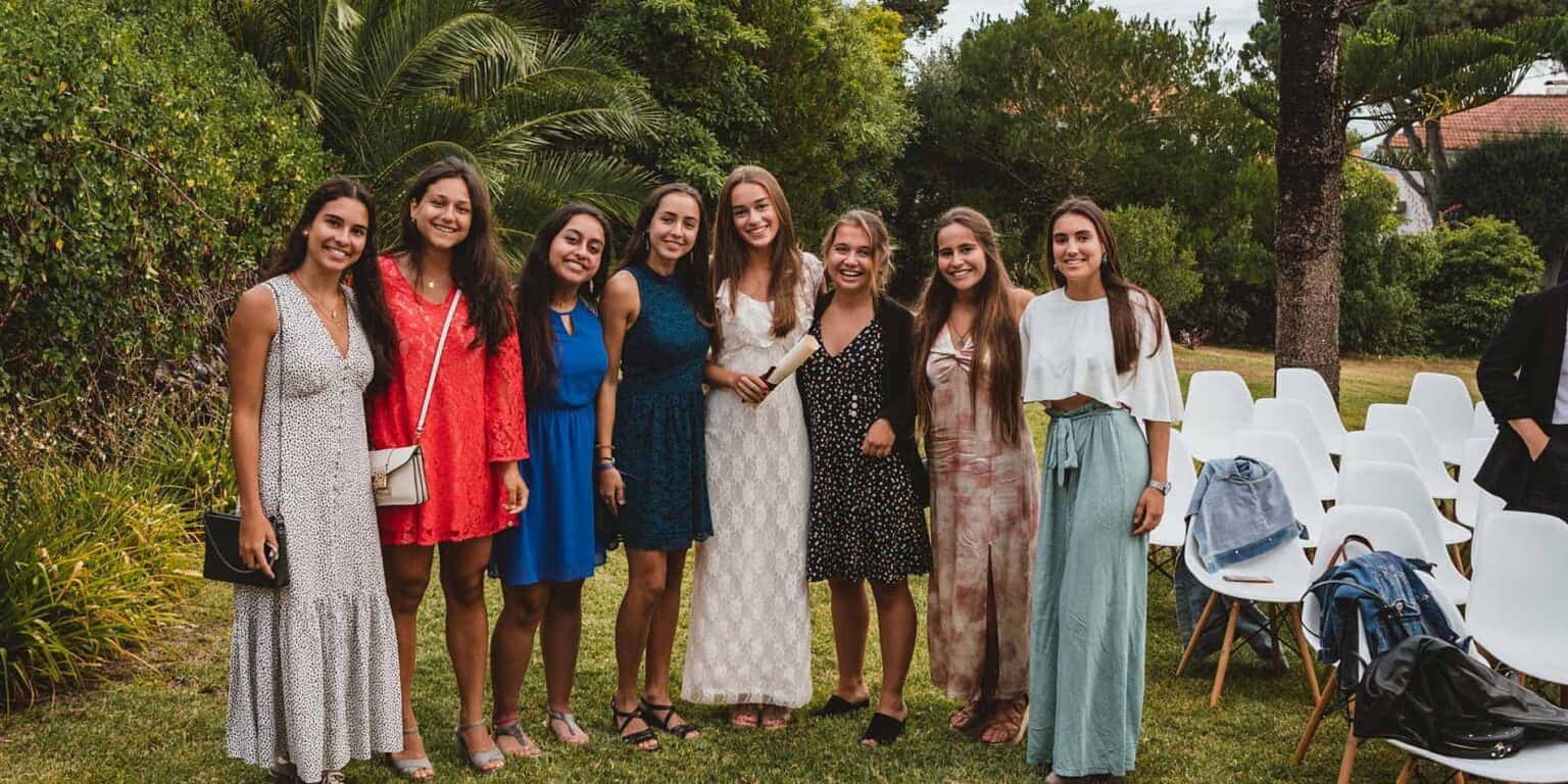 Diverse group of happy young women at outdoor school graduation or event scene with greenery.