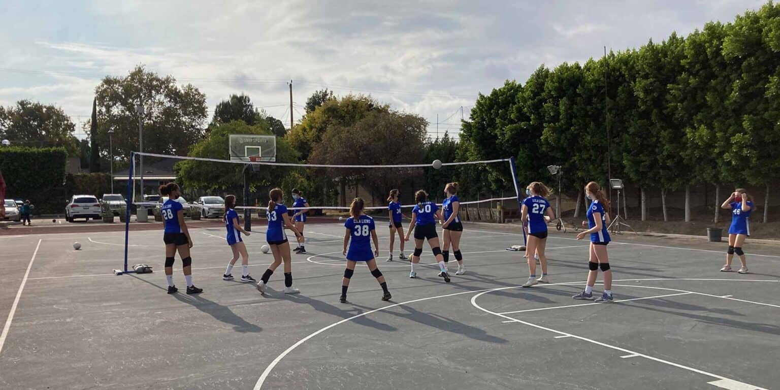 Girls volleyball team practicing on school outdoor court for competitive sports and student-athlete development.
