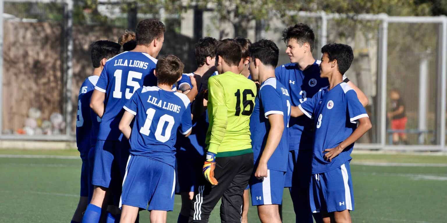 Youth soccer team huddle during match at World Schools sports event, promoting teamwork and athletic excellence.