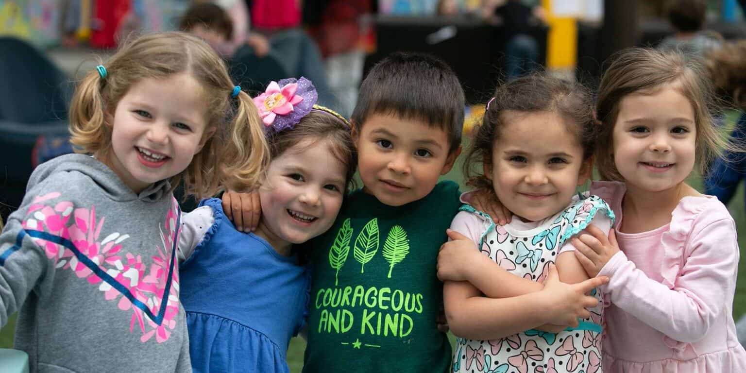 Smiling young children embracing outdoors, representing diverse backgrounds, at a World Schools education event.