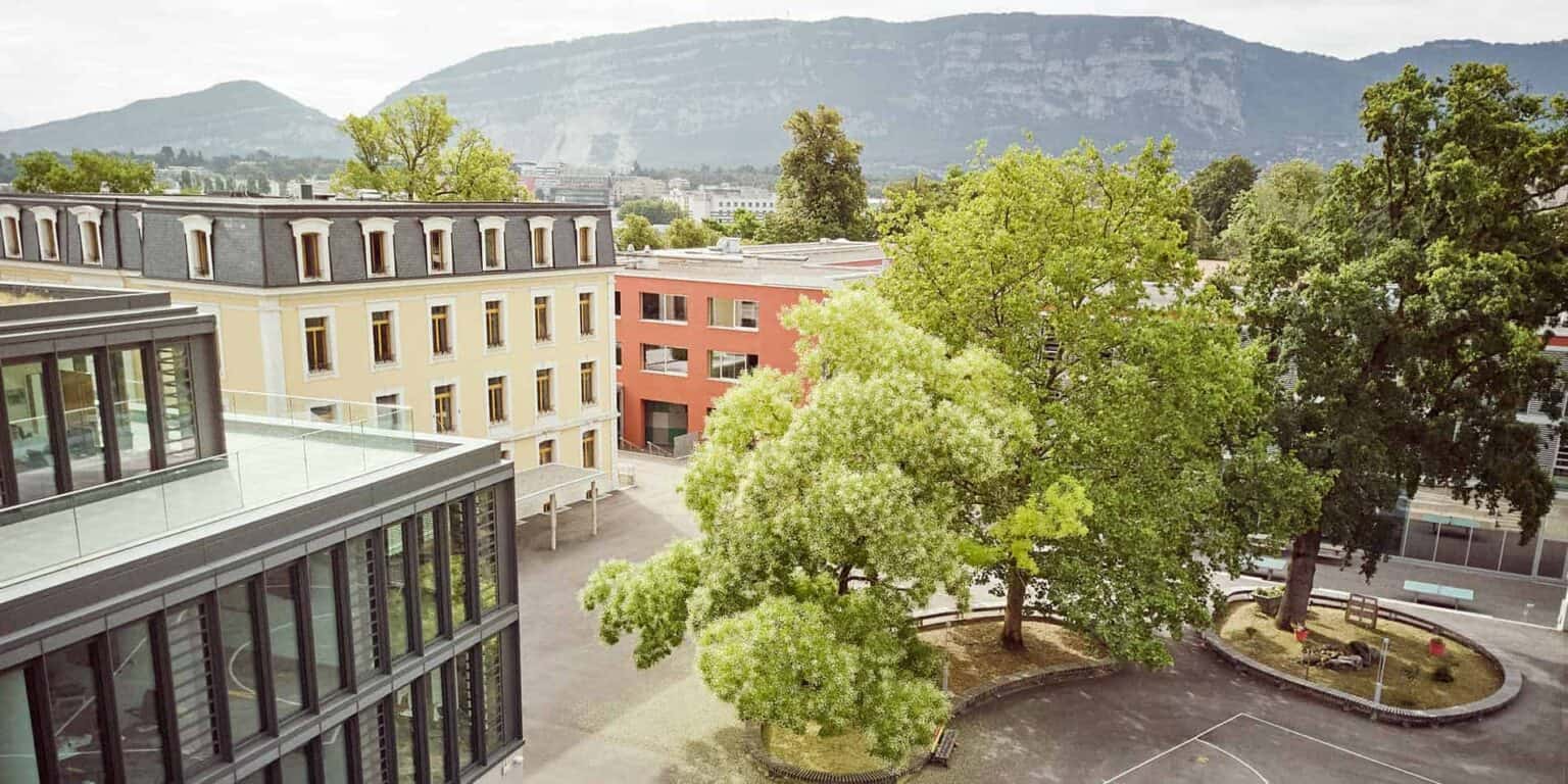 Vibrant school campus surrounded by lush green trees with mountains in the background, showcasing a prime location for international students.