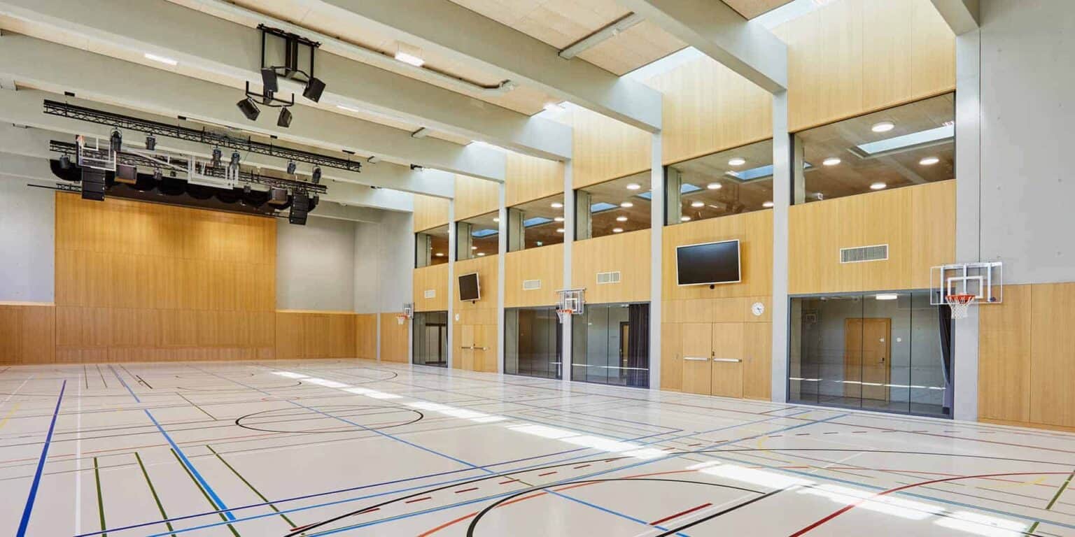 Modern school gymnasium with basketball hoops and multiple TV screens for student activities and sports.