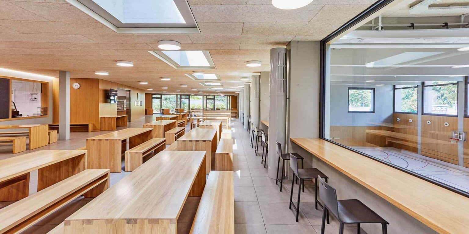 Bright modern school cafeteria with large windows and wooden furniture, promoting healthy student dining experiences.