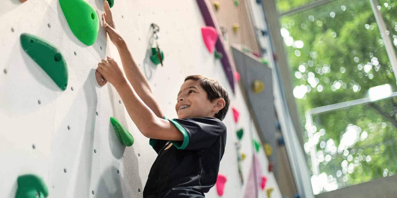Young boy climbing indoor rock wall at school, promoting youth fitness and coordination.