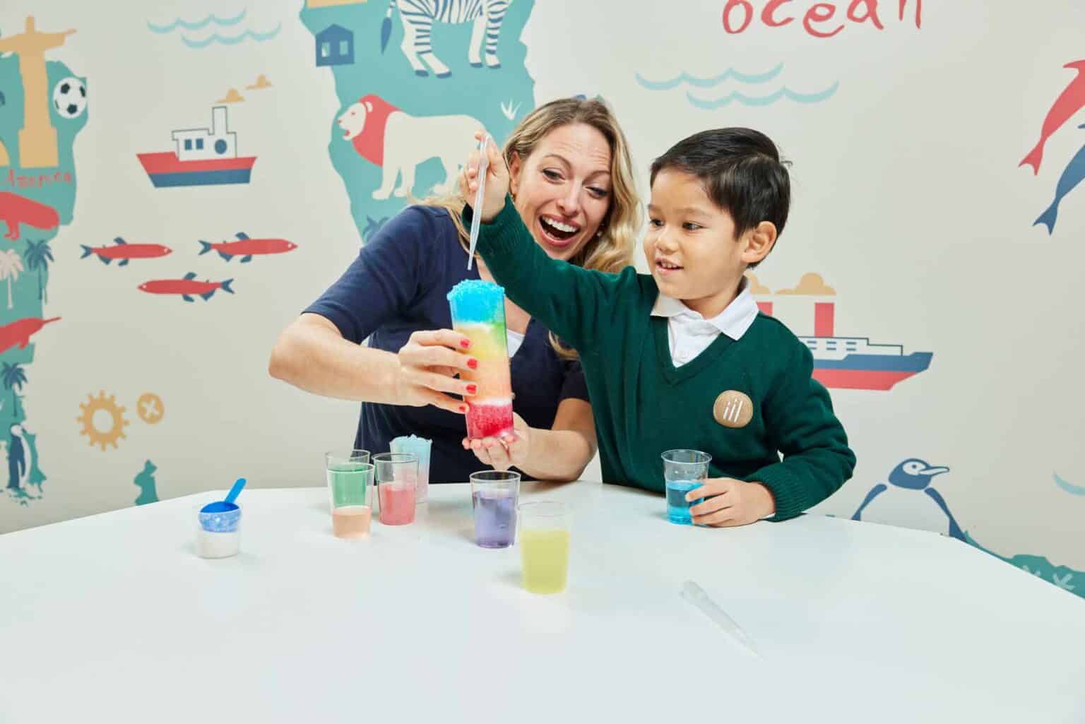 Bright young student and teacher enjoying fun science experiment with colorful liquids.