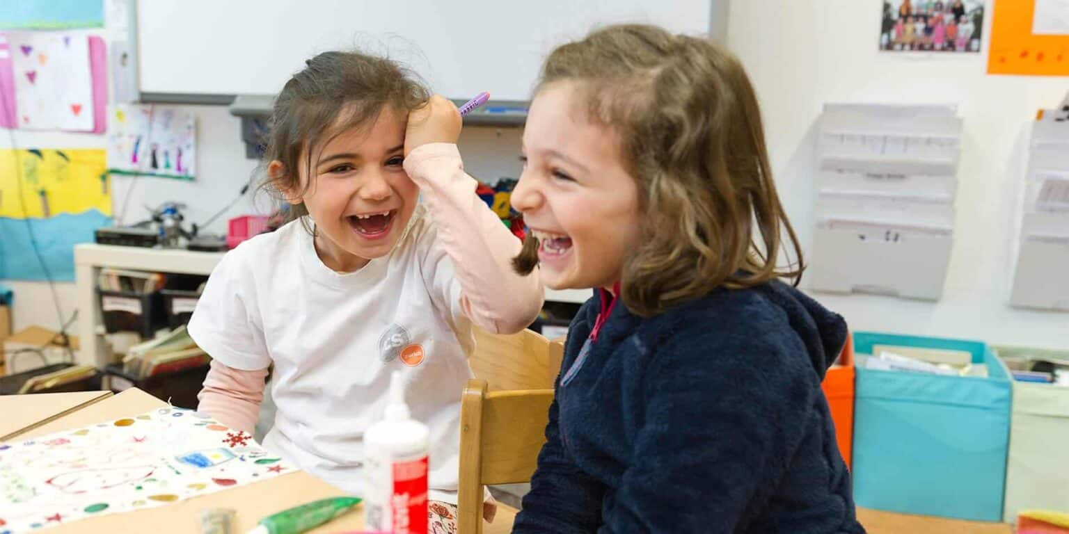Bright young girls laughing and playing in a lively school classroom.