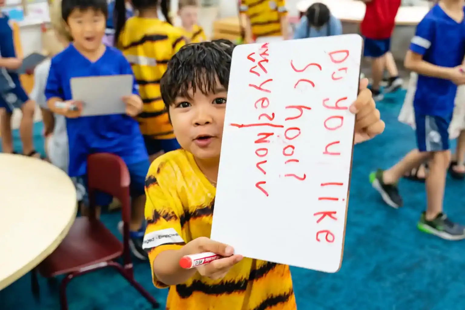 Bright smiling child holding a whiteboard with handwriting during school activity at World Schools.