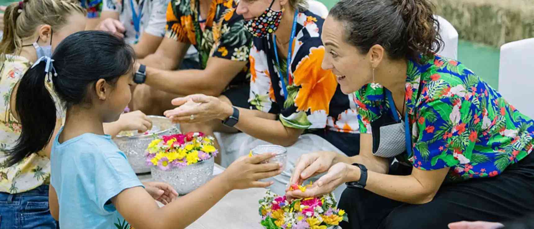 Bright schoolgirls engaging in outdoor flower craft with caring adult teachers at a vibrant school event.